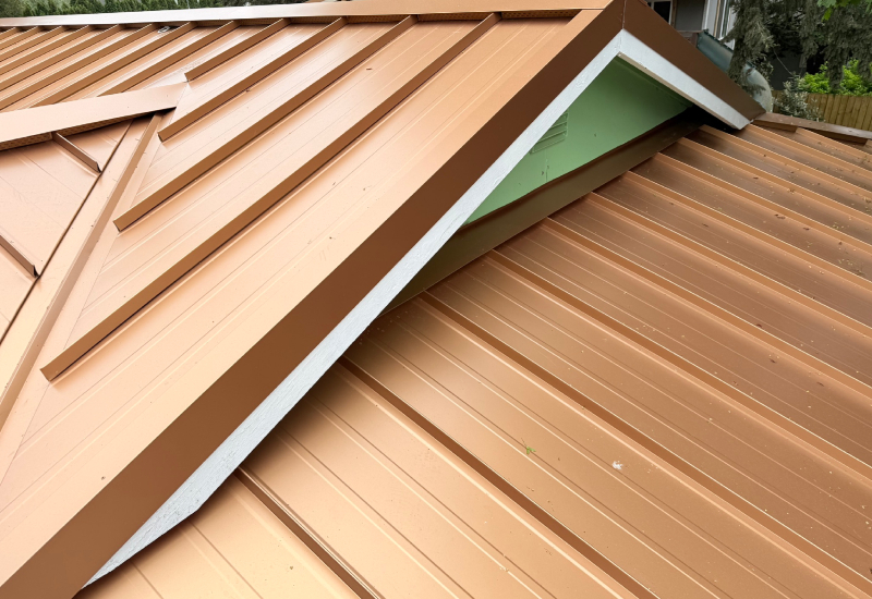 Close-up showing the standing seam panels, intersecting rooflines, and matching metal ridge and hip flashing