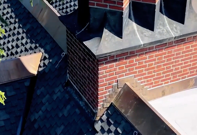 Close-up of custom copper chimney flashing and counterflashing surrounded by Owens Corning Woodmoor shingles in Granite
