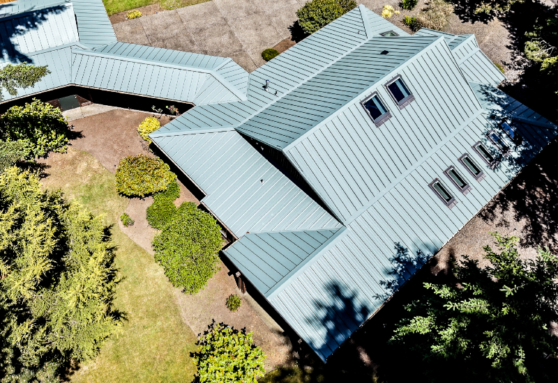 Overhead aerial view of the completed Imperial Metals standing seam metal roof in Hemlock Green, highlighting the home's complex rooflines and skylight placement.