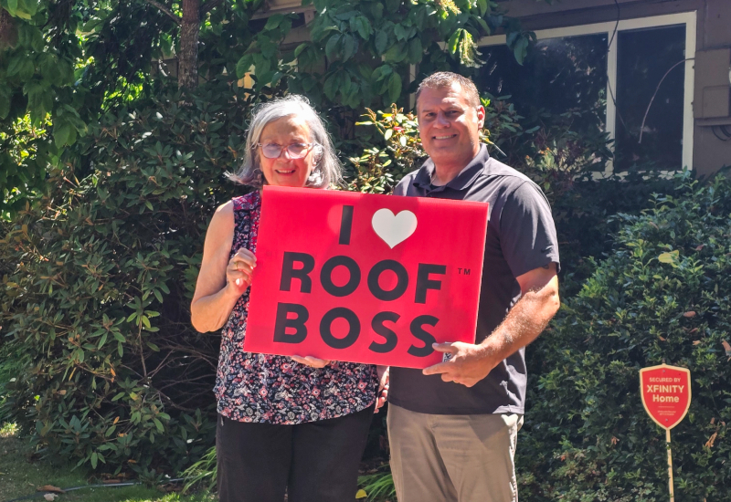 ROOF BOSS customer with estimator holding an 'I Love ROOF BOSS' sign after completion of the roofing project